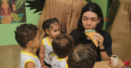 Professora tocando flauta de pã para crianças do Infantil I