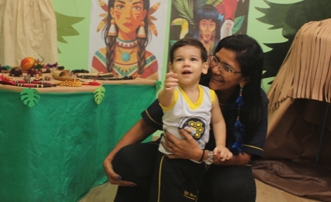 Professora segurando criança em frente aos painéis da exposição indígena