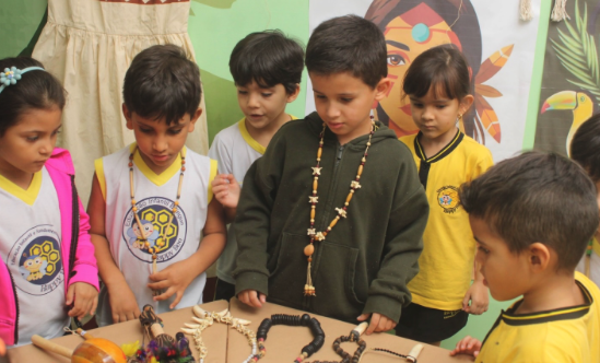Crianças observando colares e objetos artesanais na exposição indígena